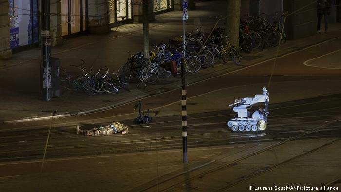 Ein Mann in Camouflage liegt neben einem Polizeiroboter auf der Straße