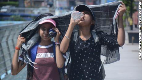 Zwei junge Mädchen bedecken ihre Köpfe, während sie in der sengenden Nachmittagshitze in Mumbai, Indien, spazieren gehen und Wasser trinken.